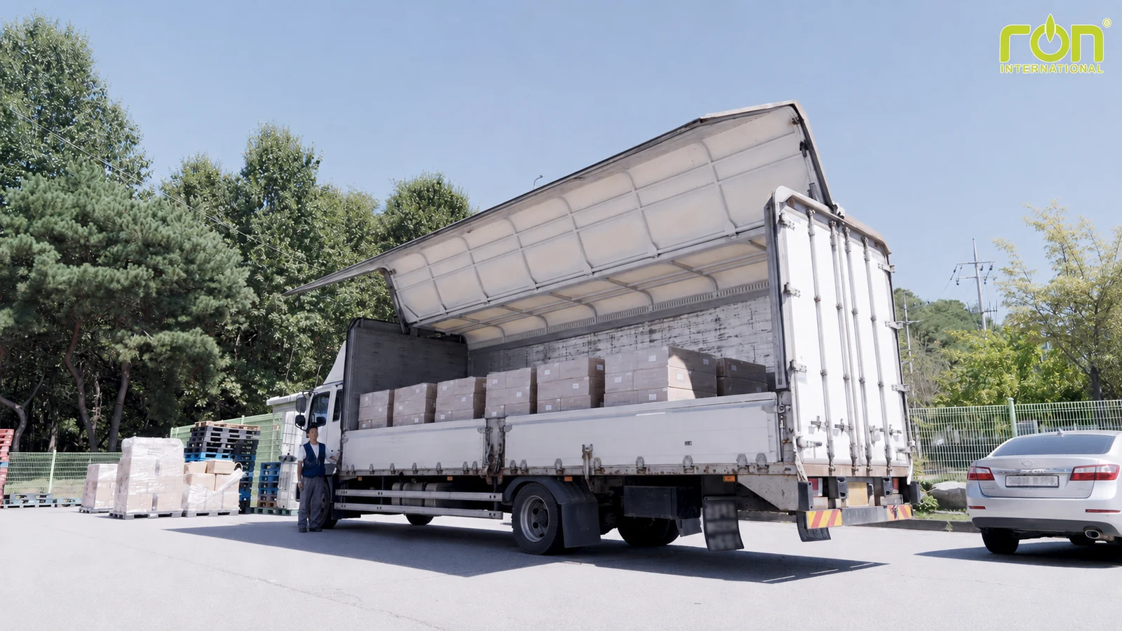 Xe tải mở thành thùng, bên trong xếp nhiều thùng carton; một người đứng cạnh cabin.