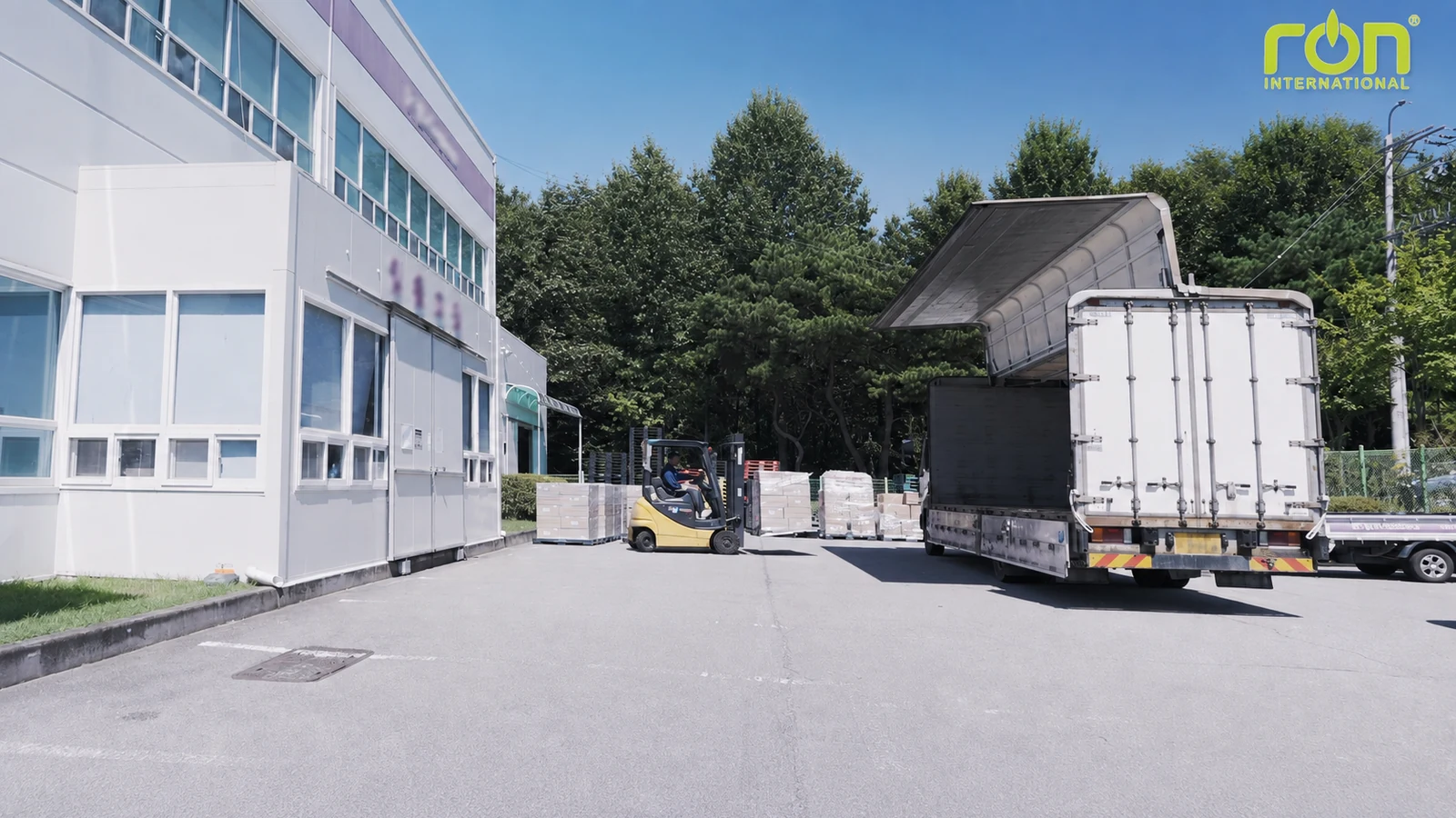 Xe nâng và xe tải mở thùng cạnh các pallet hàng trước tòa nhà.