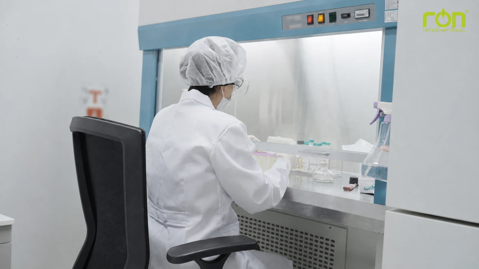 Nhân viên mặc đồ bảo hộ thao tác tại bàn thí nghiệm có vách kính.