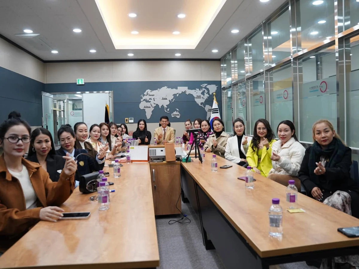 Nhóm người ngồi hai bên bàn họp dài, chụp ảnh trong phòng có vách kính và bản đồ thế giới trên tường.