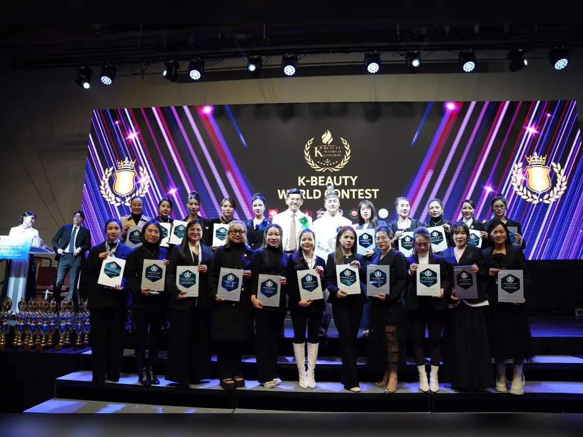 Nhóm người đứng thành hai hàng cầm bảng ghi nhận trước màn hình K-Beauty World Contest.