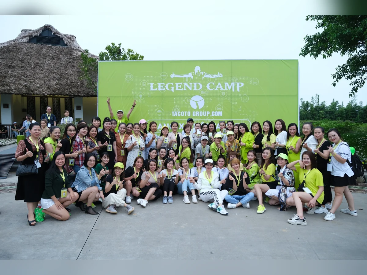 Nhóm người chụp ảnh ngoài trời trước phông nền Legend Camp của TACOTO Group.