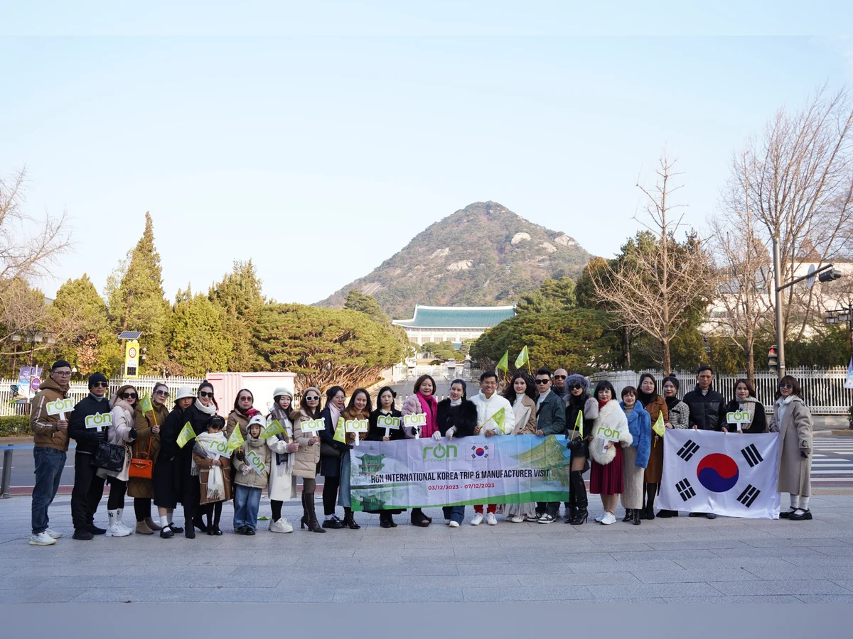 Đoàn người cầm băng-rôn RON INTERNATIONAL Korea Trip và cờ Hàn Quốc chụp ảnh ngoài trời.