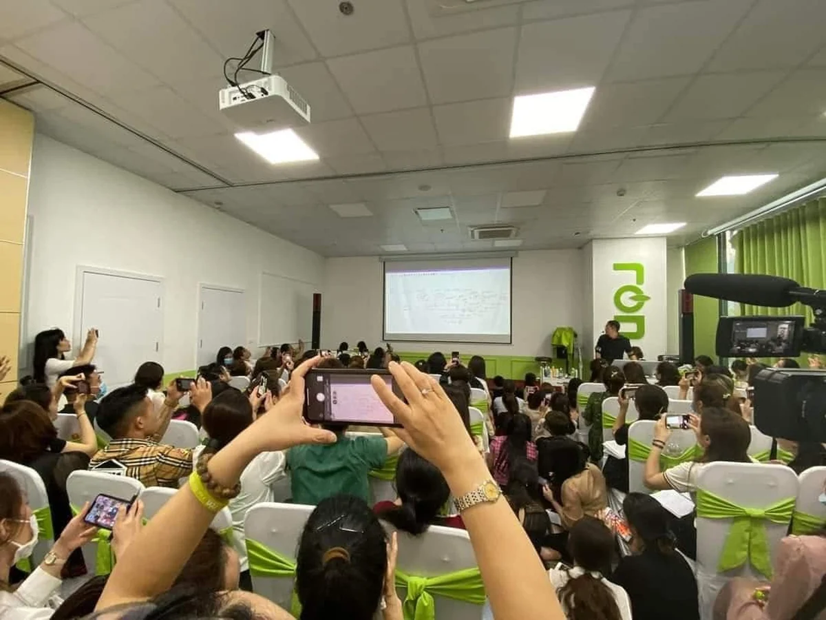 Nhiều người dùng điện thoại ghi hình diễn giả trước màn chiếu trong phòng có logo RON.