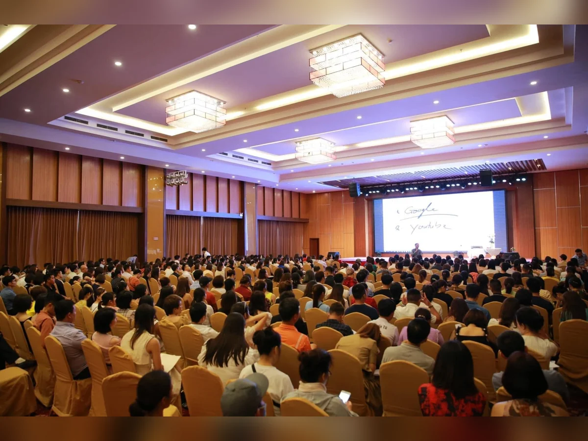 Đông người tham dự ngồi hướng về diễn giả và màn hình có các chữ Google, YouTube trong hội trường.