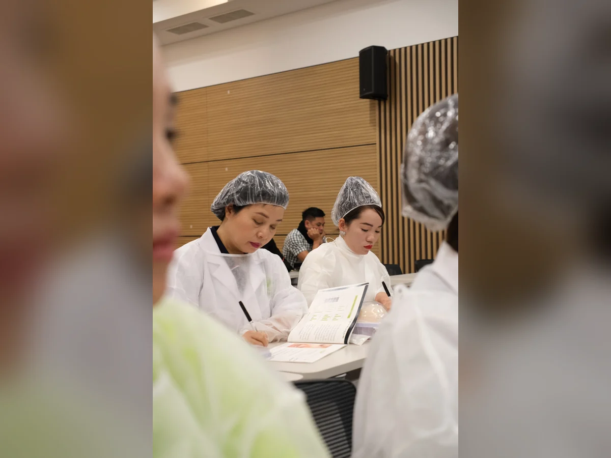 Hai người mặc áo choàng và đội mũ trùm tóc đọc tài liệu, ghi chép tại bàn.
