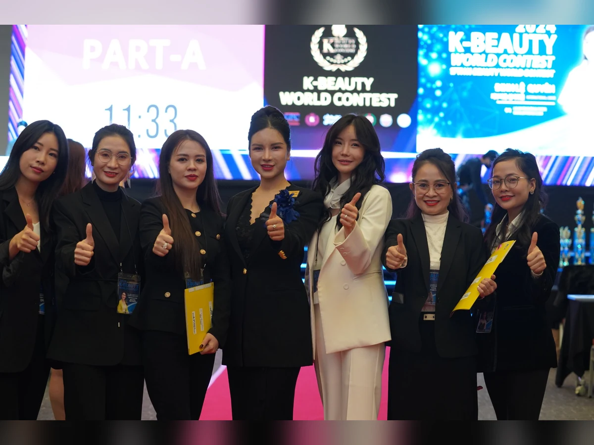 Nhóm người cầm hồ sơ và giơ ngón tay cái trước màn hình K-Beauty World Contest 2024.