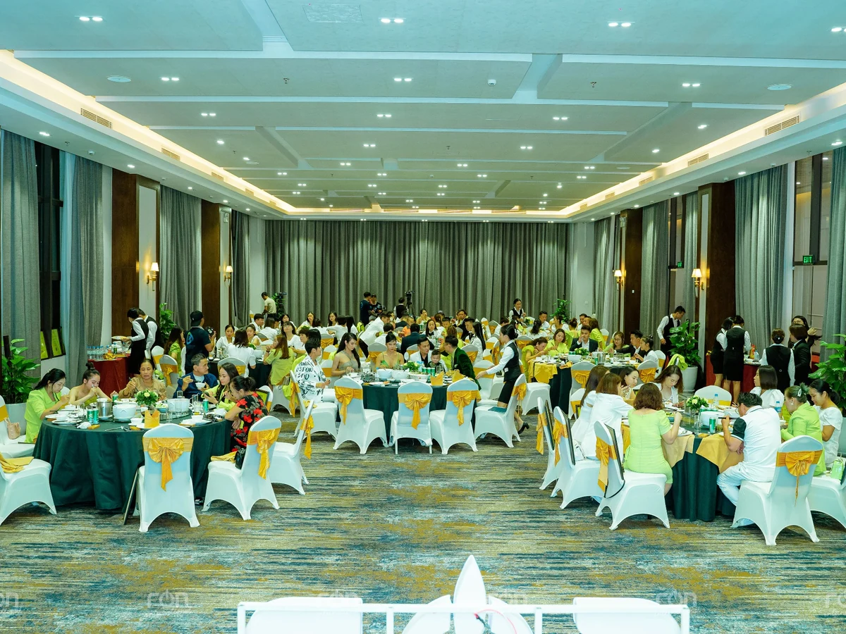 Người tham dự ngồi dùng bữa tại các bàn tròn trong phòng tiệc, giữa các nhân viên phục vụ.