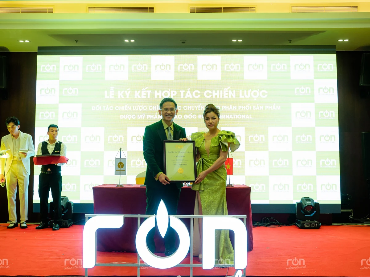 Hai người cùng cầm khung Certificate of Appreciation trên sân khấu RON INTERNATIONAL.
