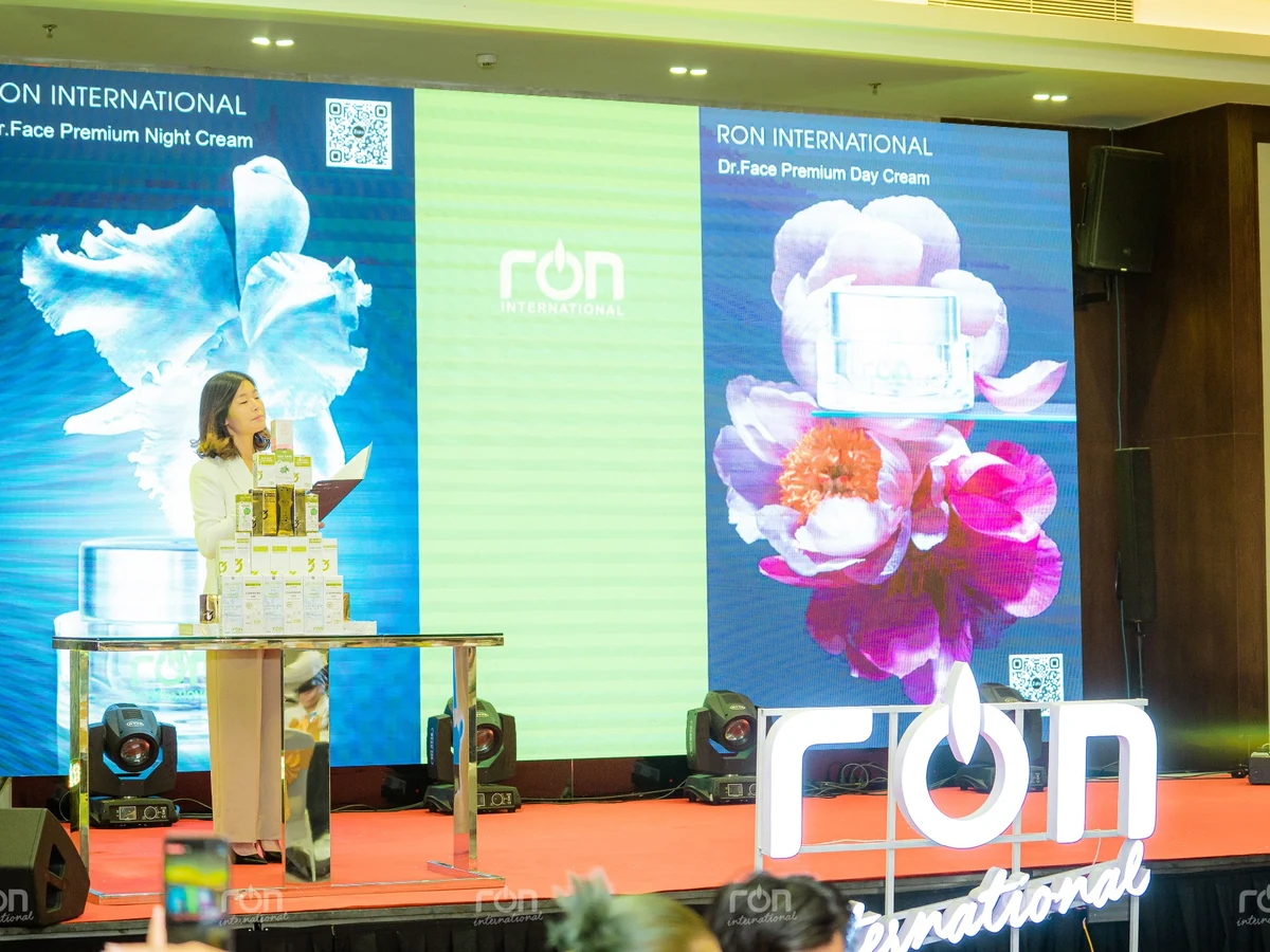 Một người đứng bên các hộp sản phẩm trên sân khấu RON, phía sau là màn hình giới thiệu kem ngày và kem đêm.
