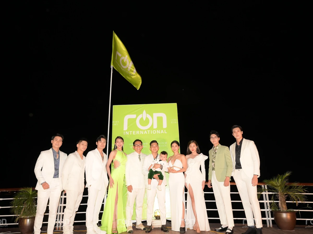 Nhóm người lớn cùng một em nhỏ chụp ảnh buổi tối trước bảng RON INTERNATIONAL.