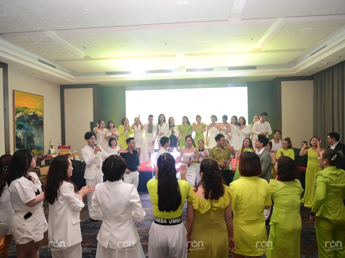 Nhóm người mặc trang phục trắng và xanh đứng giao lưu quanh những người cầm micro trước sân khấu.